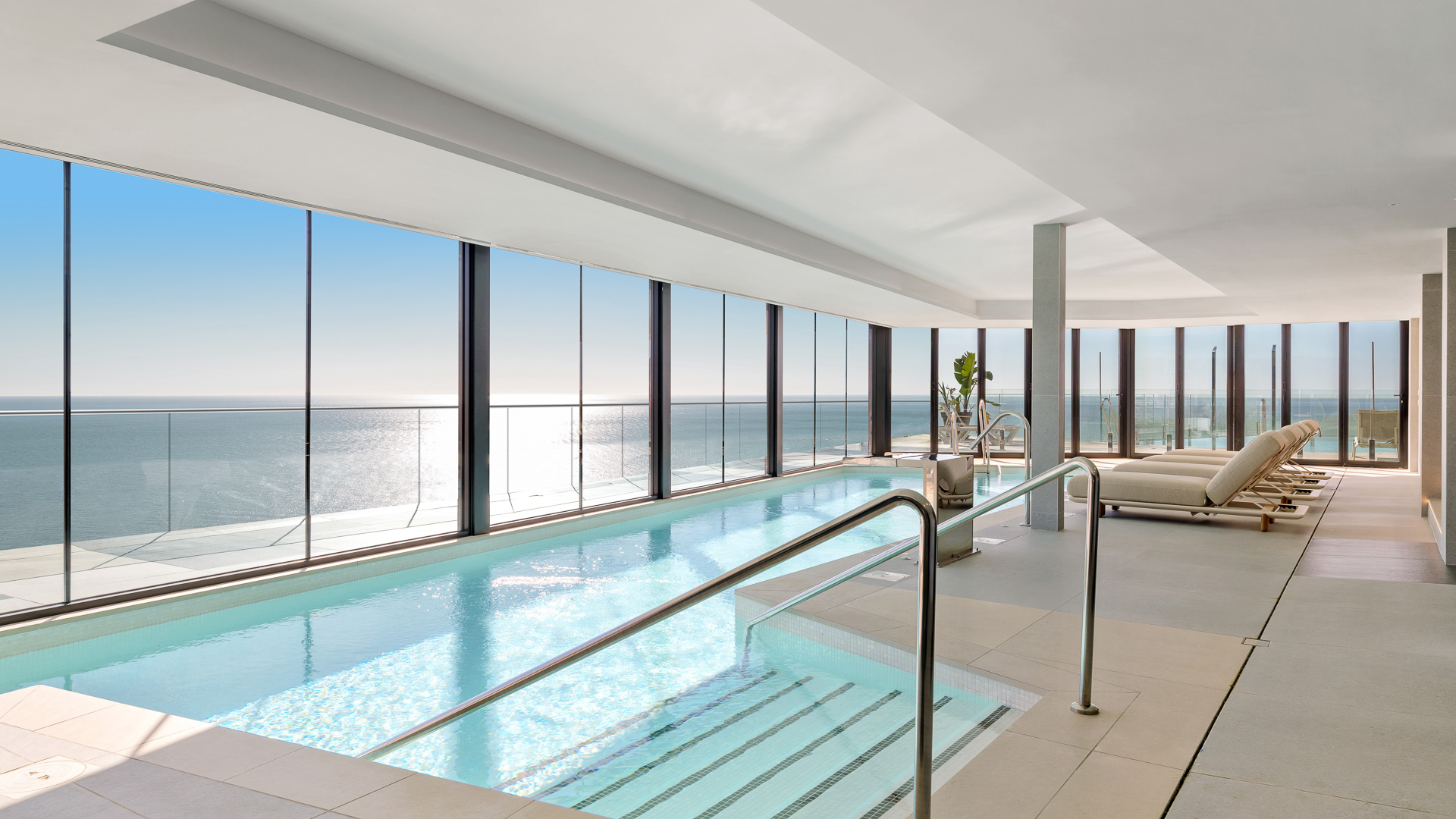 Piscina interior luminosa con grandes ventanales y zona de relax con tumbonas.