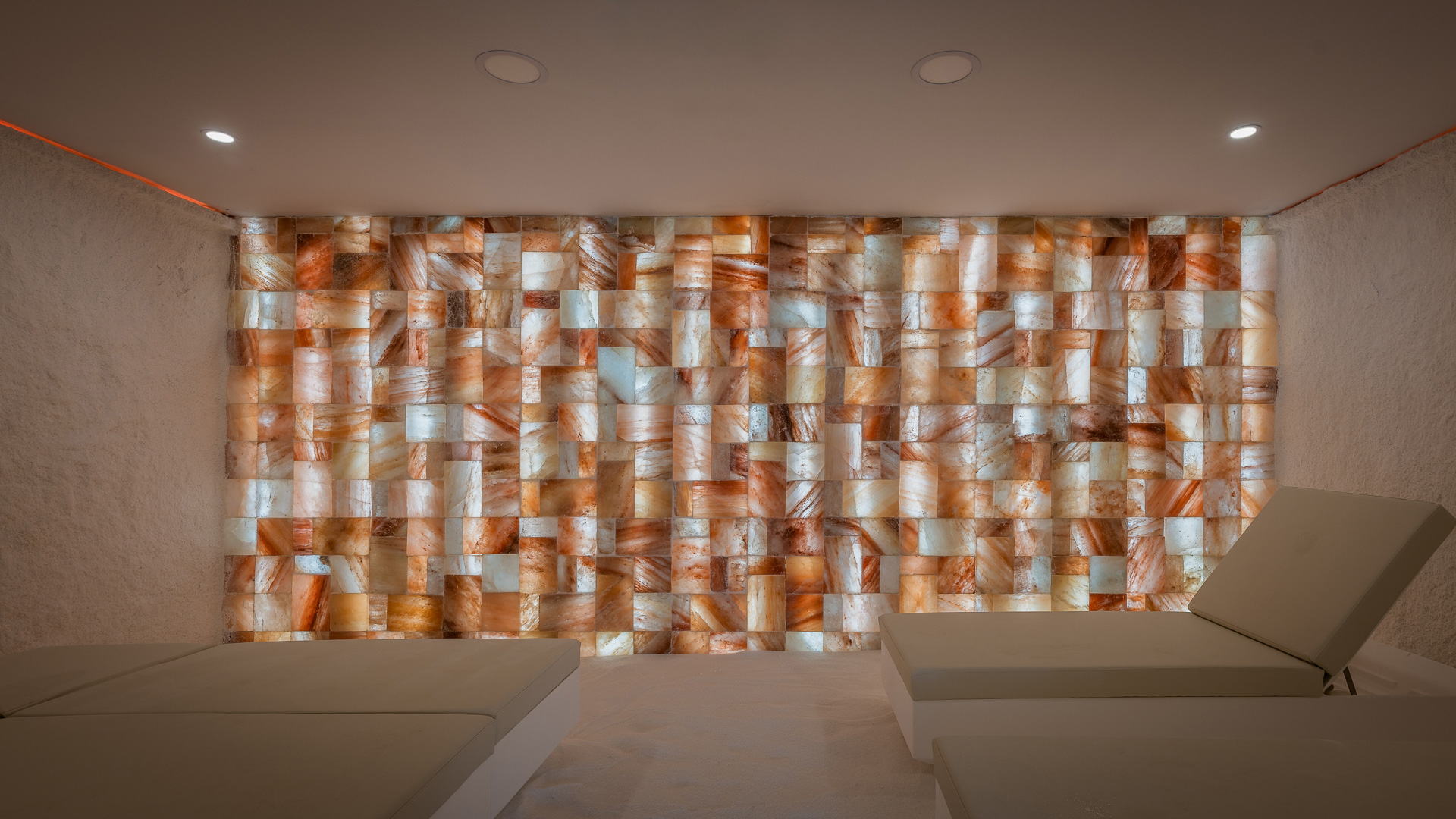 Sala de relax con varias camillas y pared de sal iluminada.