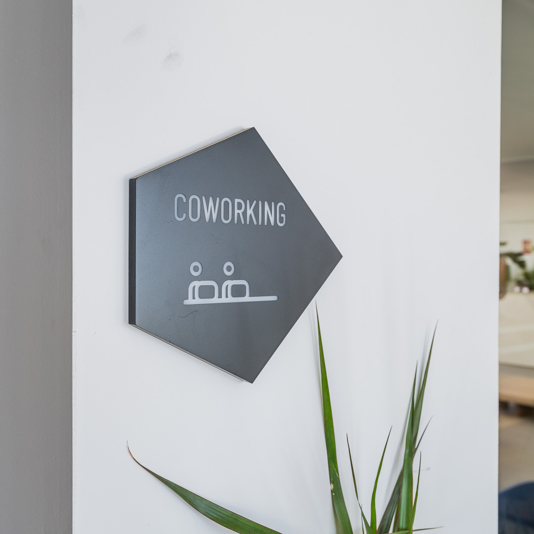 Placa negra con la palabra “Coworking”, colocada sobre una pared blanca en una zona común.
