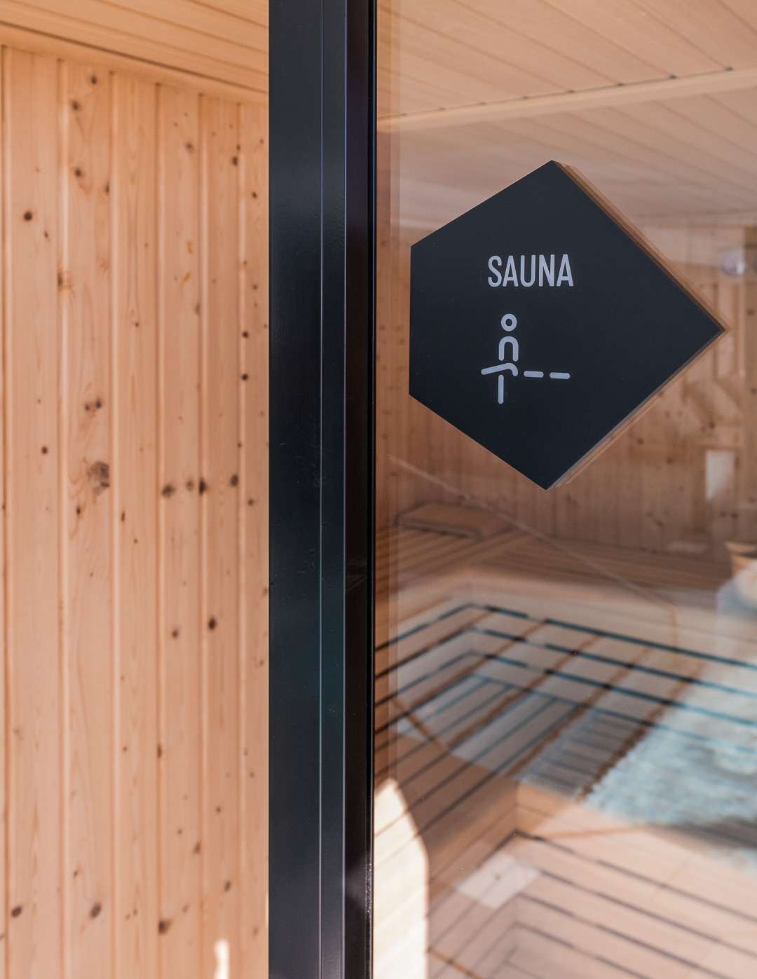 Placa negra con la palabra “Sauna” que indica la sauna, colocada sobre una pared blanca en una zona común.
