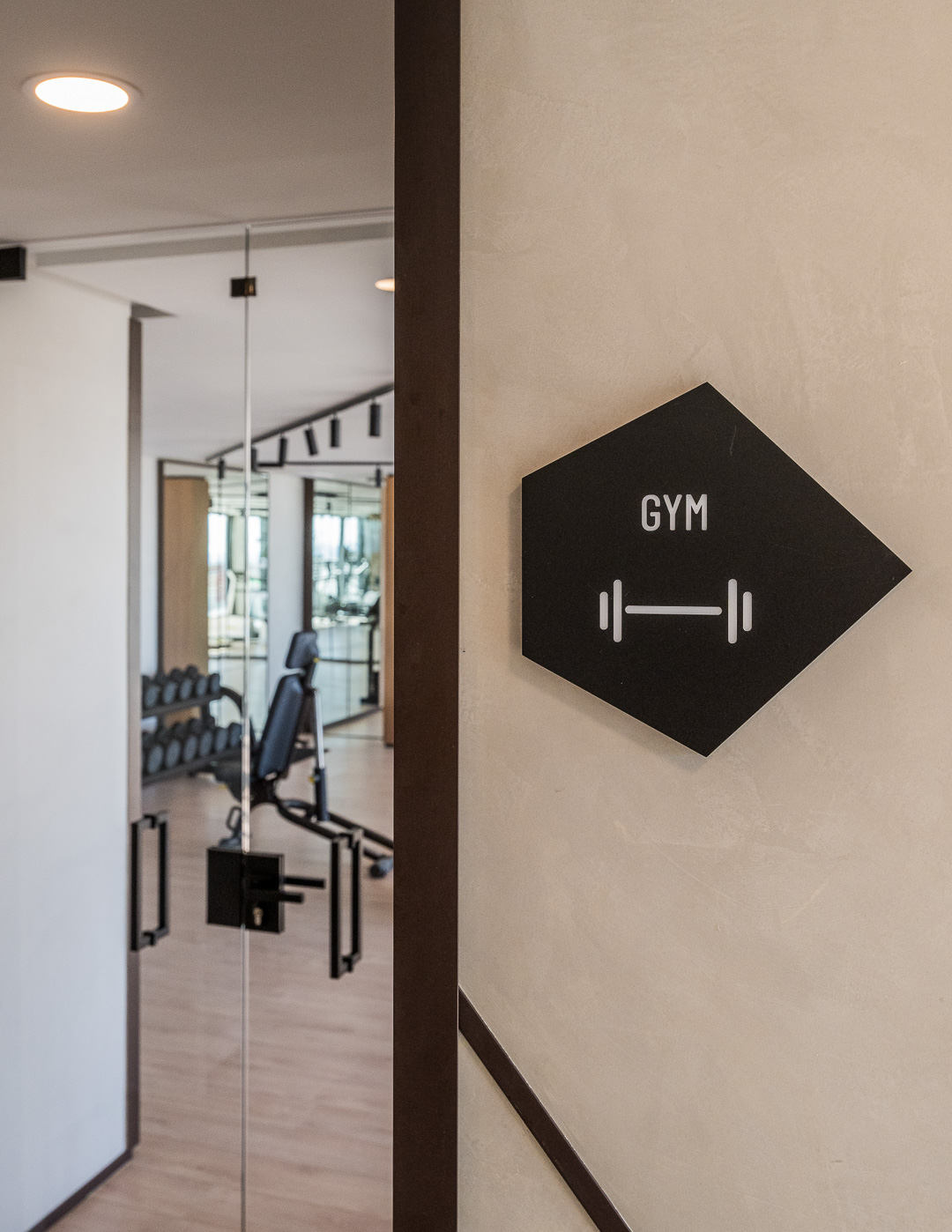 Placa negra con la palabra “Gym” que indica la presencia de un gimnasio, colocada en una pared blanca.