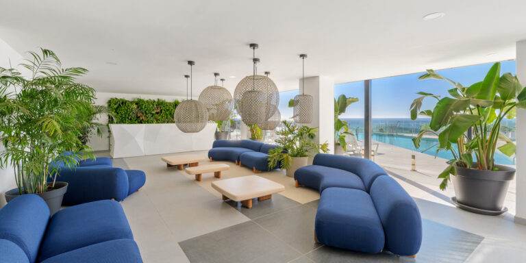 Área lounge de coworking con sofás, plantas decorativas y vistas al exterior.