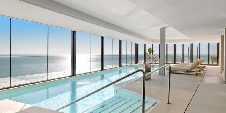 Piscina interior luminosa con grandes ventanales y zona de relax con tumbonas.