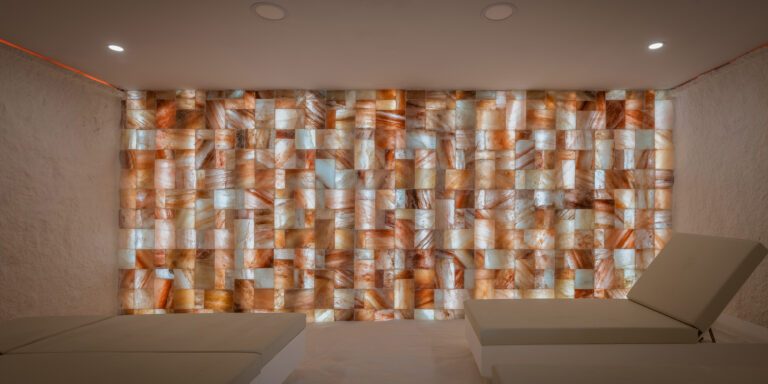 Sala de relax con varias camillas y pared de sal iluminada.