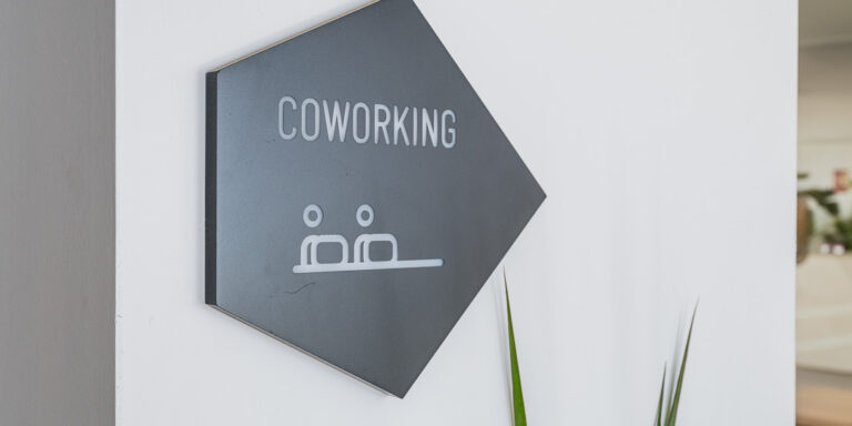 Placa negra con la palabra “Coworking”, colocada sobre una pared blanca en una zona común.