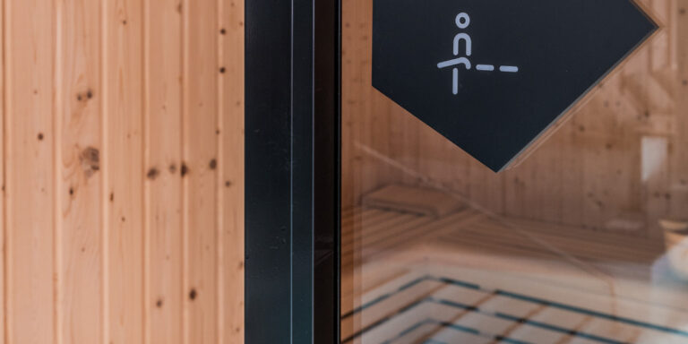 Placa negra con la palabra “Sauna” que indica la sauna, colocada sobre una pared blanca en una zona común.